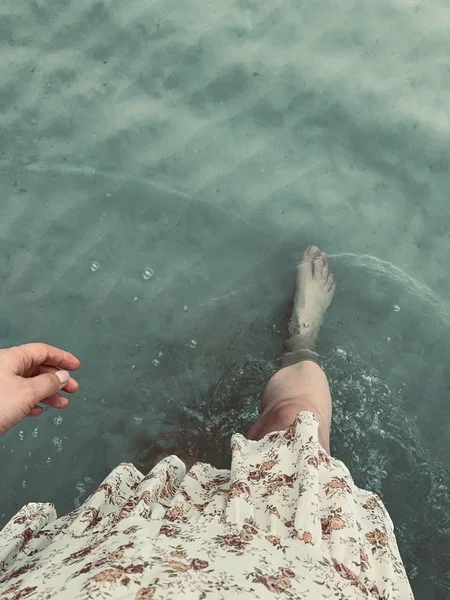 Girls foot and hand walking in the ocean on sand, shot from the top view. Can see dress and a hand