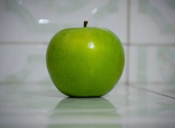 Messa a fuoco selettiva di una mela verde su una superficie riflettente — Foto Stock