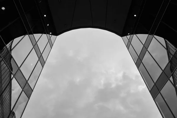 Fotografía de ángulo bajo a escala de grises de las ventanas de espejo de un edificio moderno y el cielo nublado detrás —  Fotos de Stock