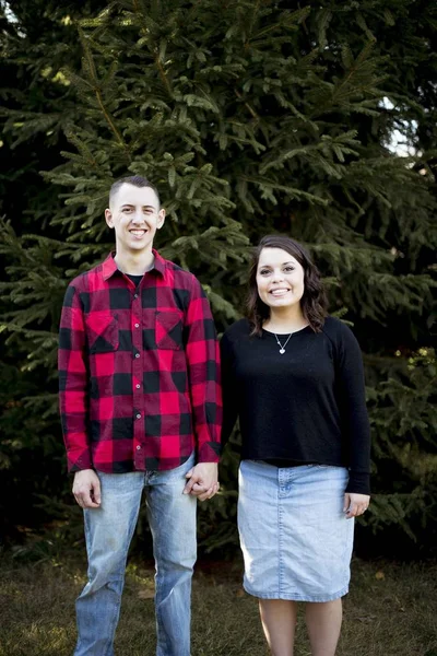 Vertical shot of a young couple holding hands while standing in front of a big tree — ストック写真