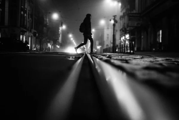 Снимок в серой шкале человека, переходящего улицу ночью — стоковое фото
