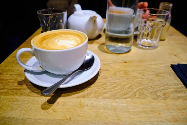 Ένα φλιτζάνι καφέ και μερικά άδεια ποτήρια και μια τσαγιέρα σε ένα ξύλινο τραπέζι. — Φωτογραφία Αρχείου