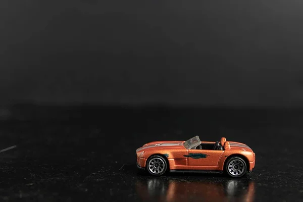 Foco seletivo tiro de um carro de brinquedo laranja com listras de prata em uma superfície preta — Fotografia de Stock