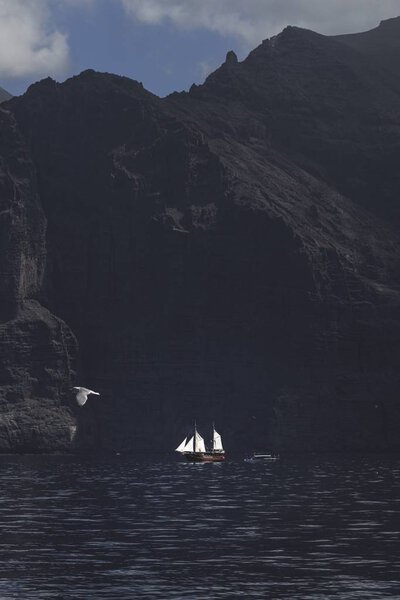 Vertical shot of a sailboat at the rock formation in the calm ocean Stock Photo