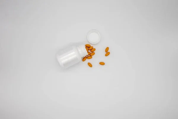 白い背景に白い丸薬瓶からこぼれるオレンジの丸薬 — ストック写真