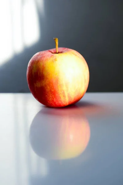 Fechar de uma maçã vermelha refletindo sobre a mesa sob as luzes com um fundo embaçado — Fotografia de Stock