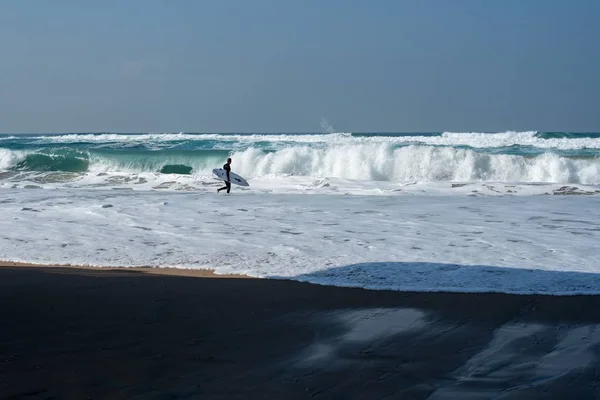 Landschap van een strand omringd door de golvende zee met een surfer erin onder een blauwe hemel — Stockfoto