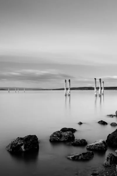 Vertical Greyscale Shot Wooden Pier Rock Formations Cloudy Sky — 스톡 사진