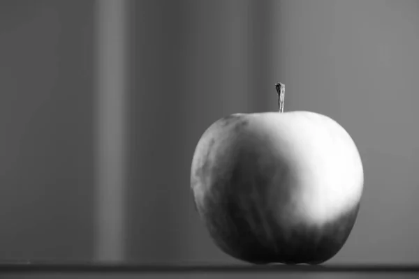 Escala de cinza de uma maçã refletindo sobre a mesa com um fundo embaçado — Fotografia de Stock