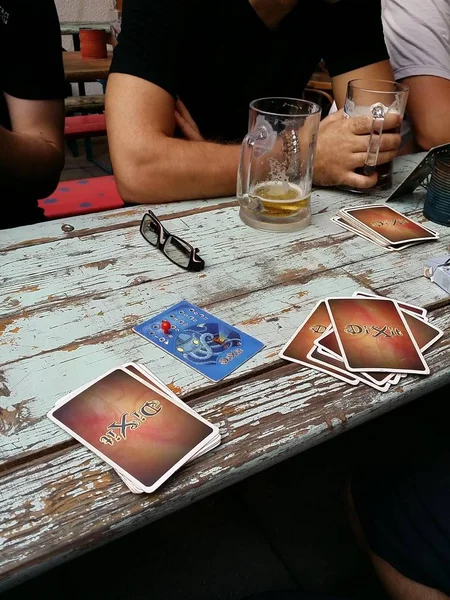 Budapest, Hungary - 2015.08.06.: Dixit spelen met vrienden op een oud houten bureau tijdens het drinken — Stockfoto