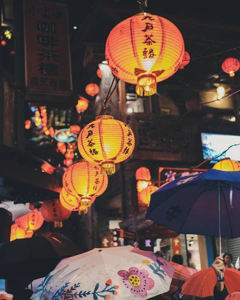 Tiro vertical de pessoas andando ao redor com guarda-chuvas sob lanternas de papel à noite — Fotografia de Stock