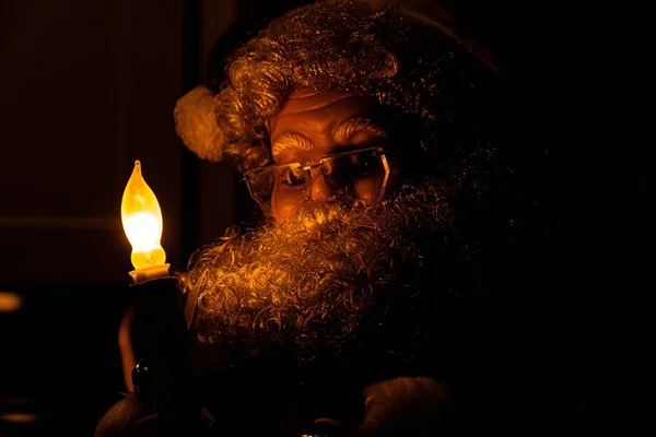 Closeup of a Santa Claus doll in front of a fake lit candle in a dark room — Stock Photo, Image