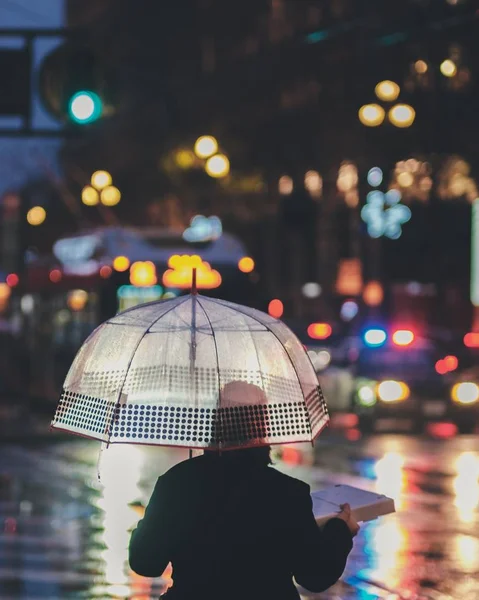 Вертикальний знімок людини, що стоїть під парасолькою в дощовий день — стокове фото