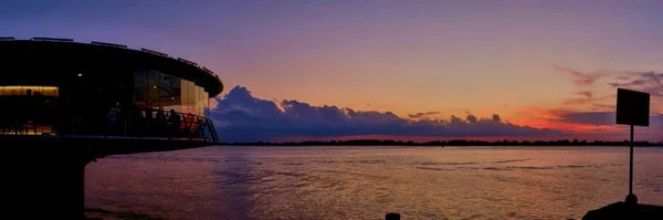 Tiro panorâmico de uma varanda redonda de vidro sobre o oceano calmo sob o belo céu colorido — Fotografia de Stock