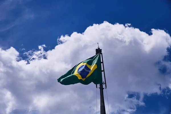 Foto de bajo ángulo de la bandera de Brasil bajo las hermosas nubes en el cielo azul. — Foto de Stock