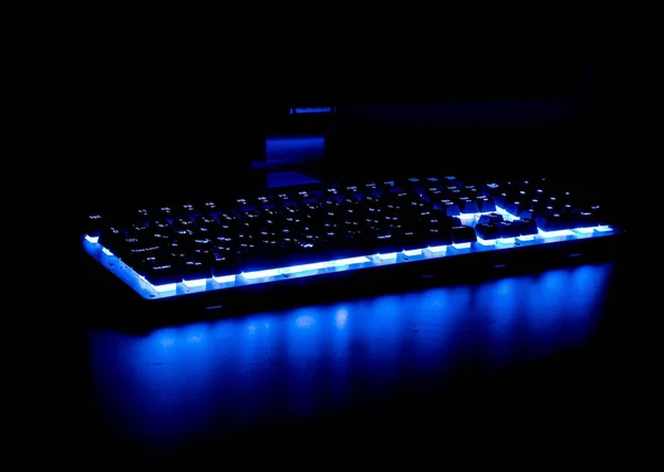 Gros plan d'un clavier bleu éclairé par LED dans une pièce sombre — Photo