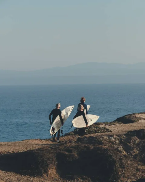 Vue verticale de surfeurs marchant en tenant leur planche avec la mer au loin — Photo