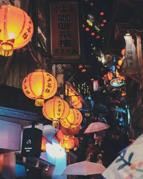 Vertikale Aufnahme von Menschen, die nachts mit Regenschirmen unter Papierlaternen spazieren — Stockfoto