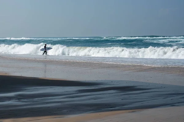 Пейзаж пляжа в окружении моря с серфером с доской рядом с ним — стоковое фото