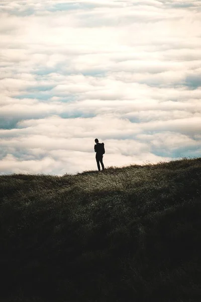 Siluet seseorang berdiri di atas bukit berumput dengan langit mendung di latar belakang — Stok Foto