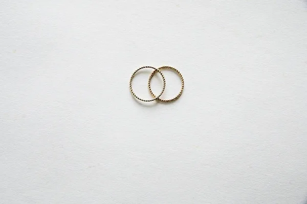 A high angle shot of a silver ring and a golden ring on a white surface