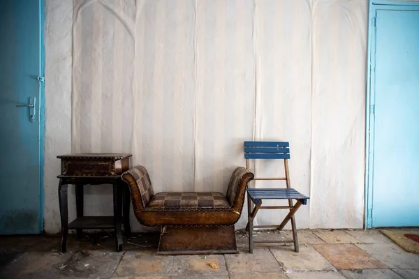 An old room with blue doors and old furniture against a white wall