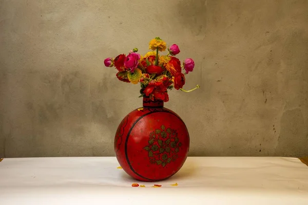 A vintage red vase with red and orange peonies in front of an old wall