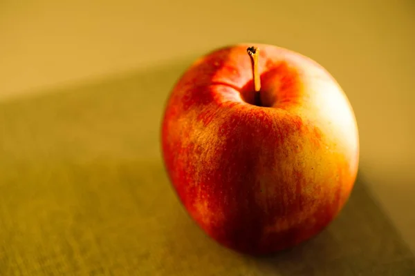 Fechar de uma maçã vermelha refletindo sobre a mesa sob as luzes com um fundo embaçado — Fotografia de Stock