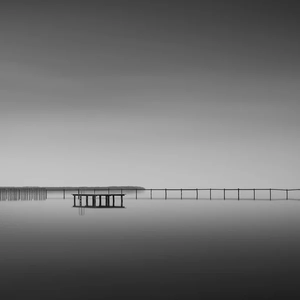 在美丽多云的天空下 一个靠近大海的木制码头的灰白色镜头 — 图库照片