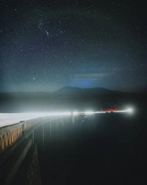 Vertical shot of a bridge with a silhouette of a mountain in the distance under a galaxy sky — 스톡 사진