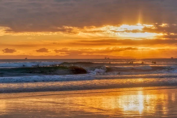 Playa rodeada por el mar ondulado bajo un cielo nublado durante una puesta de sol dorada — Foto de Stock