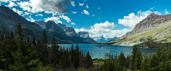 Largo tiro de um lago cercado por montanhas e árvores sob um céu azul — Fotografia de Stock