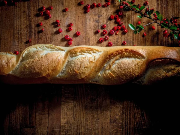 Overhead shot of a loaf of bread near red berries on a wooden surface — Stock Photo, Image