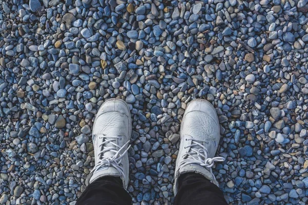 Alto angolo sparato di gambe umane in sneakers bianche in piedi sulla spiaggia di pietra — Foto Stock