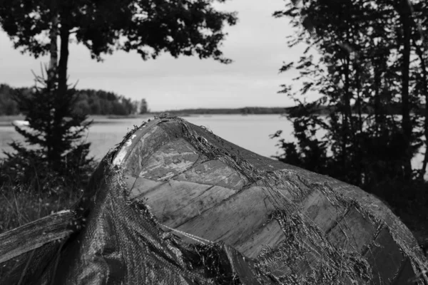 Серый снимок старой заброшенной лодки на берегу моря под чистым небом — стоковое фото