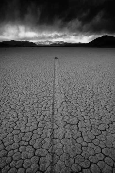 Vertical greyscale shot of a deserted ground of sand surrounded by a mountainous scenery — 스톡 사진