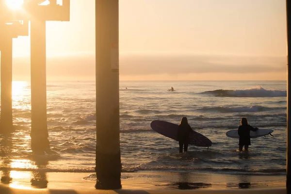 Mensen met surfplanken in de zee met de zonsondergang op de achtergrond — Stockfoto