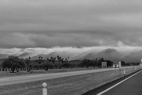 Серый снимок дороги с горами вдали под облачным небом — стоковое фото