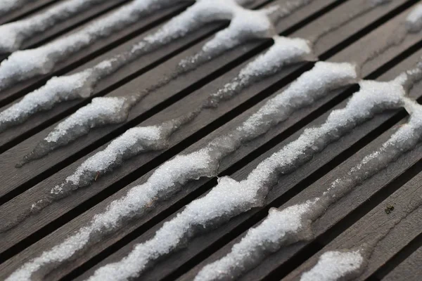 Großaufnahme von schmelzendem Schnee auf einer dunklen Holzoberfläche im Winter — Stockfoto