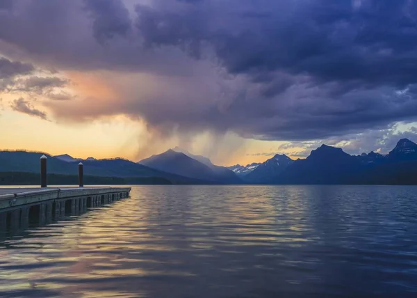 Pier de concreto perto do mar cercado por altas montanhas rochosas durante o pôr do sol — Fotografia de Stock