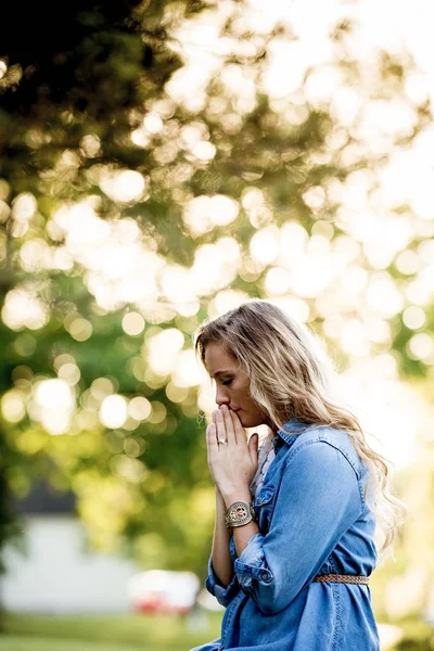 파란 드레스를 입고 햇빛 아래 정원에서 희미 한 배경으로 기도하는 여자 — 스톡 사진