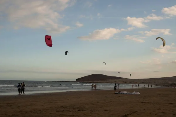 Strand omgeven door paragliders en de zee onder een bewolkte hemel tijdens de avond — Stockfoto