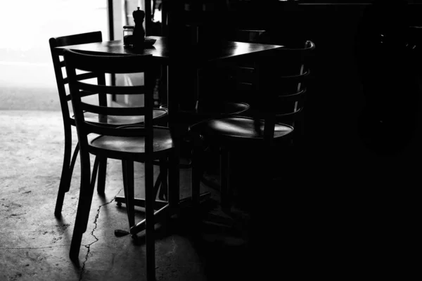 Greyscale skott av ett bord med stolar i ett mörkt rum under dagtid — Stockfoto