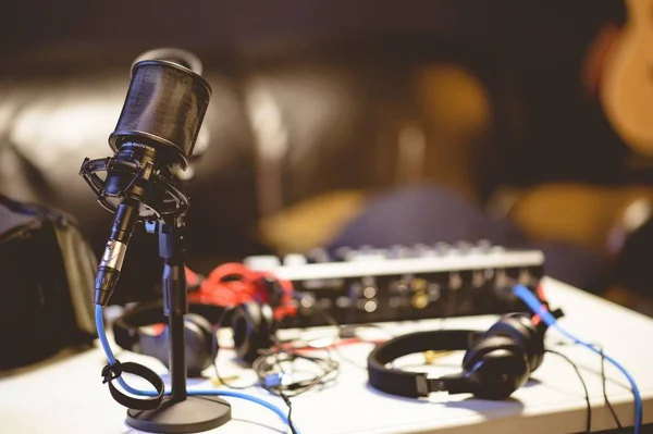 Microfone em um estúdio cercado por equipamentos sob as luzes com um fundo embaçado — Fotografia de Stock