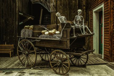 An old wooden carriage with skeletons and pumpkins on it in a building clipart