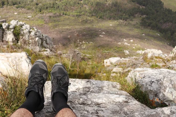 Людина зі спортивним взуттям сидить на скелі і розслабляється — стокове фото
