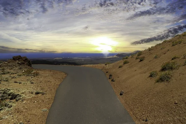 Road surrounded by hills covered in greenery and sand under a cloudy sky during the sunset in Spain — Stock Photo, Image