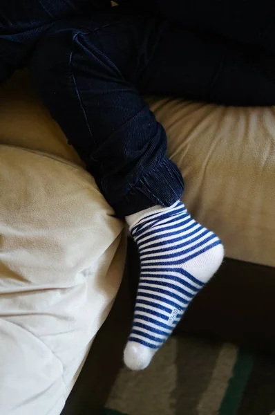 Vertical shot of a person sitting on a couch with striped socks — Stock Photo, Image