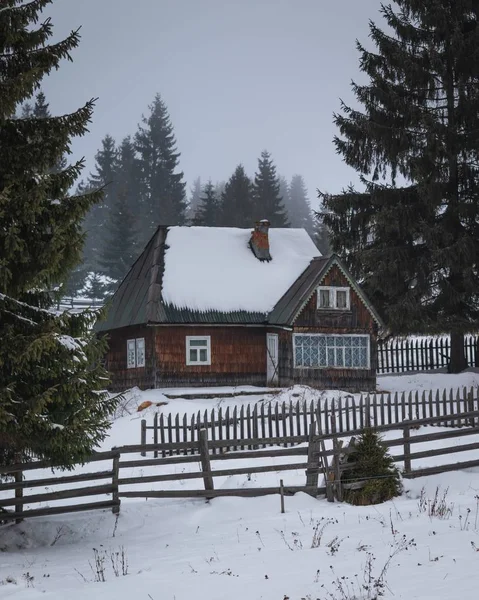 Casa con valla de madera en medio de la nieve y los pinos. — Foto de Stock