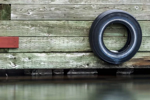 Roda preta de um carro preso a uma parede de madeira acima da água — Fotografia de Stock